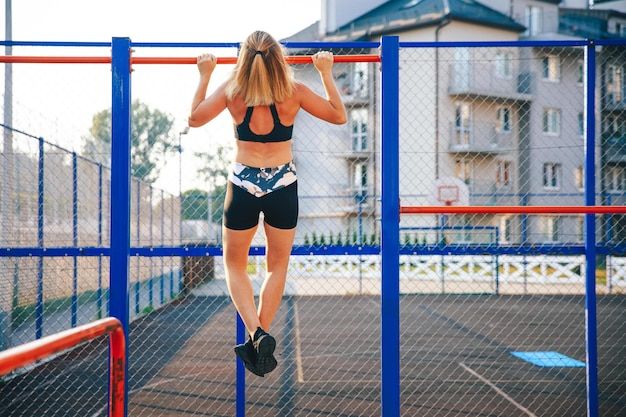 Young woman pulling up with crossed legs on horizontal bars Free Photo