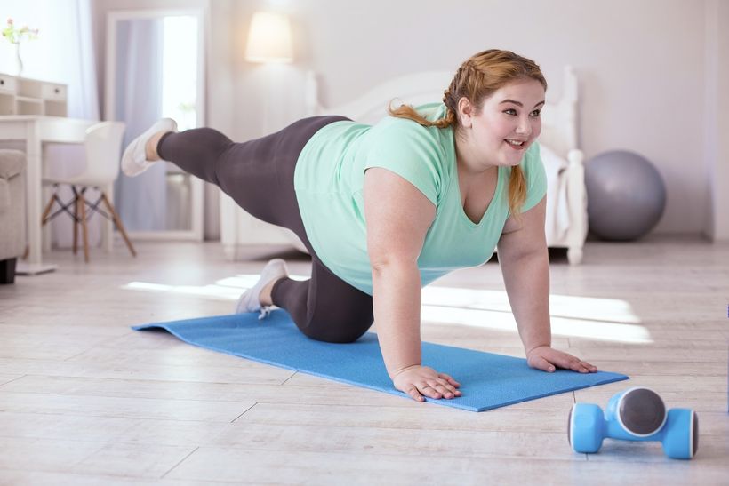 Žena s nadváhou cvičící na podložce na cvičení