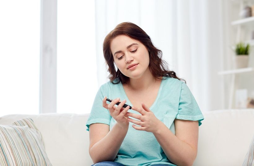 Žena sediaca na gauči si meria hladinu cukru v krvi
