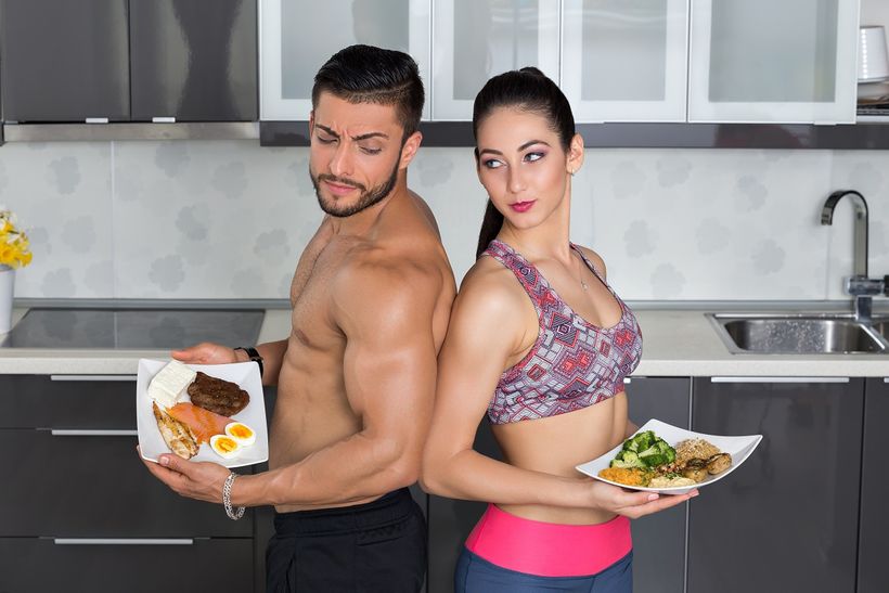 Sportovně vypadající pár muže a ženy v kuchyni držící dva talíře se zdravým jídlem.