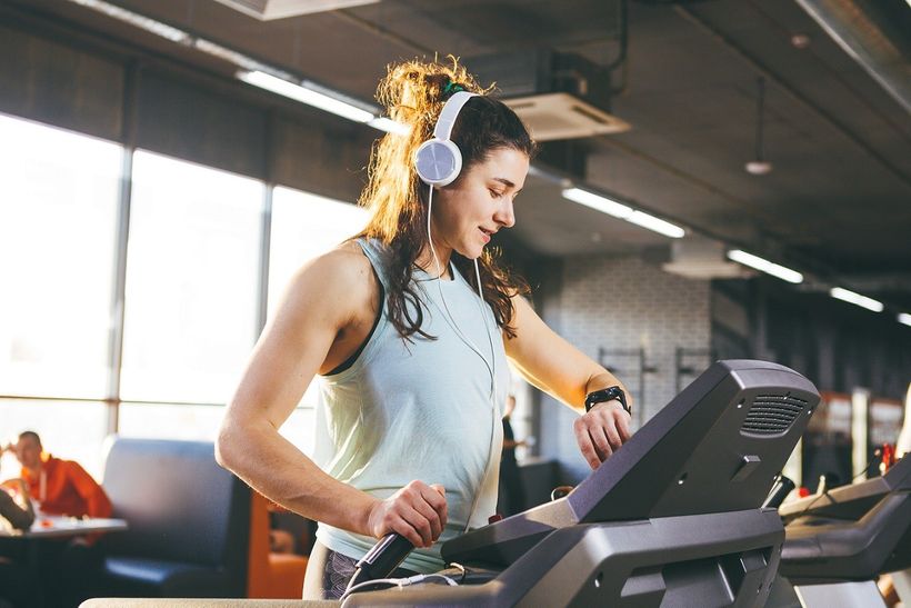Žena na běžícím pásu kontrolující výšku své tepové frekvence na fitness hodinkách